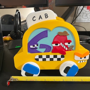 Puede incluir: Un taxi de juguete amarillo con un patrón de cuadros blanco y negro en el lateral. El taxi tiene un personaje morado y rojo en el interior y la palabra "CAB" en la parte superior. El taxi tiene ruedas azules y negras.