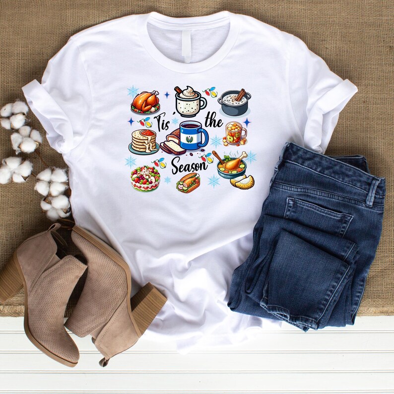 May include: White t-shirt with a festive design featuring various holiday foods and the text "Tis the Season".