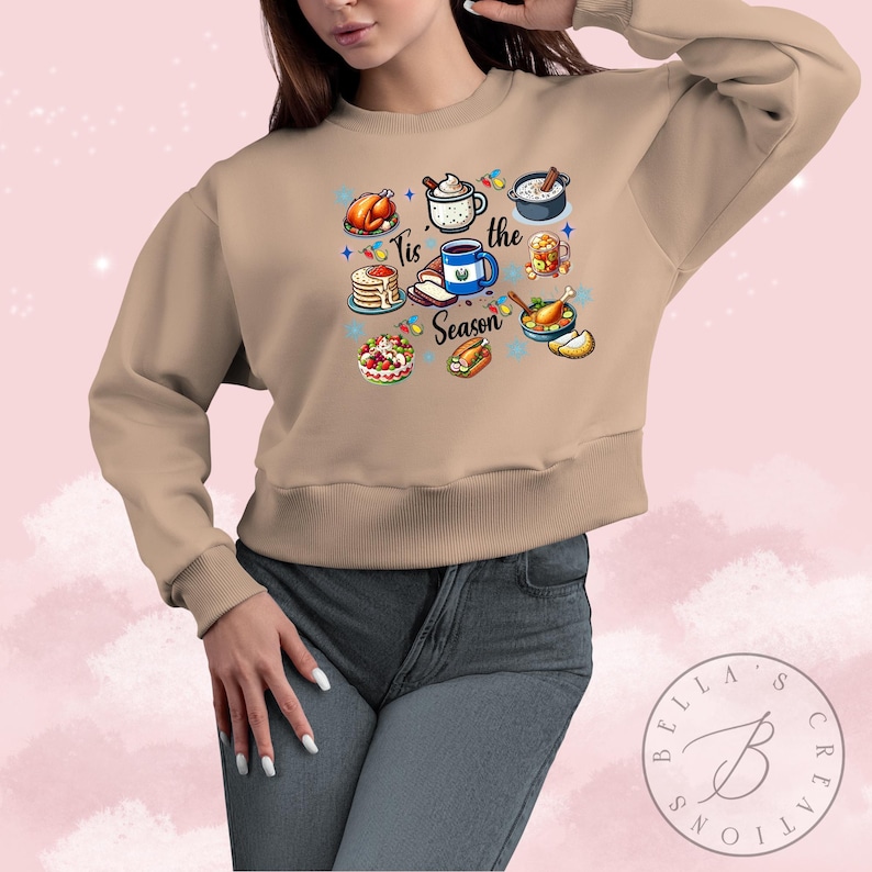May include: A tan sweatshirt with a graphic print of various holiday foods and the text "Tis the Season".