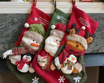 May include: Three red and green Christmas stockings with different characters. The stocking on the left has a snowman and penguin, the middle stocking has Santa Claus, and the right stocking has a reindeer and a snowman. Each stocking has the text "Merry Christmas Custom your design images/text" embroidered on it.