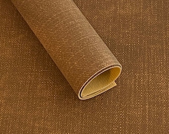 May include: A roll of brown faux leather fabric with a subtle woven texture. The fabric is rolled up and the edge of the roll is visible.