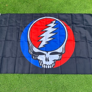 May include: A black flag featuring a colourful Grateful Dead Steal Your Face logo. The logo is a red, white and blue circle with a skull and lightning bolt design.