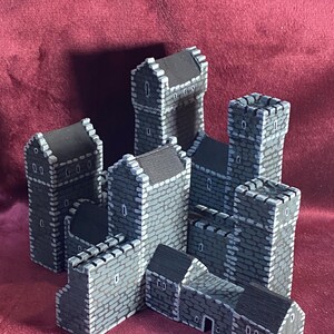May include: A set of grey stone castle buildings with black roofs. The buildings are made of cardboard and are designed for tabletop gaming.