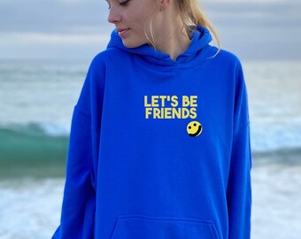 May include: A vibrant blue hoodie with a front pocket and a drawstring hood. The hoodie displays the text "LET'S BE FRIENDS" in yellow, accompanied by a yellow smiley face. The garment is made from a soft fabric.