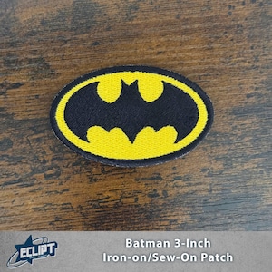 May include: A 3-inch Batman logo patch. The patch features a black bat symbol within a yellow oval border. The patch is designed to be ironed on or sewn onto fabric. The patch is on a wooden surface.
