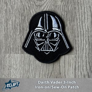 Puede incluir: Un parche termoadhesivo/para coser de Darth Vader de 7,6 cm en blanco y negro. El parche presenta un contorno detallado del casco y la máscara de Darth Vader. El parche está sobre una superficie de madera gris.