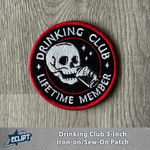 Op de afbeelding: Ronde zwarte en rode patch met een witte schedel en de tekst "DRINKING CLUB LIFETIME MEMBER". De patch heeft een diameter van ongeveer 7,6 cm.