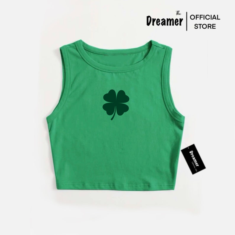 May include: Green sleeveless crop top with a four-leaf clover graphic. The Dreamer Official Store logo is on a tag attached to the shirt.