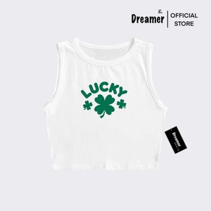 May include: White sleeveless crop top with a green shamrock and the word "LUCKY" printed on the front.