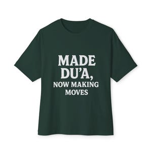 May include: A dark green t-shirt with the white text "MADE DU'A, NOW MAKING MOVES". The short-sleeved shirt is made of a soft material and is suitable for casual wear.