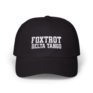 Może przedstawiać: Czarna czapka bejsbol&oacute;wka z białym haftem z napisem "FOXTROT DELTA TANGO".