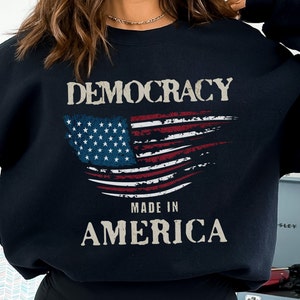 May include: Black sweatshirt with a distressed American flag design and the text "DEMOCRACY MADE IN AMERICA".