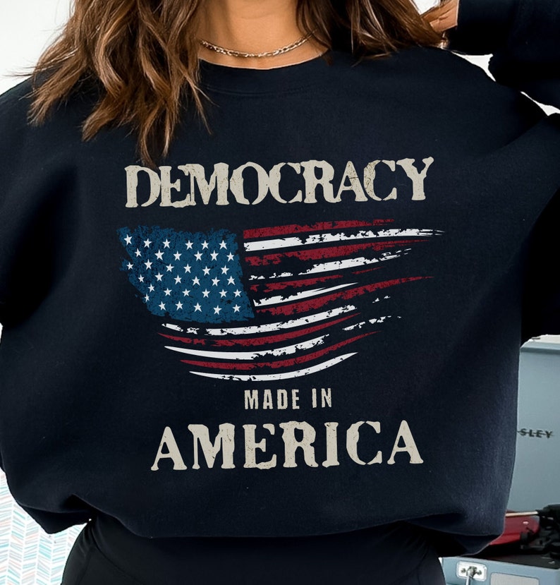 May include: Black sweatshirt with a distressed American flag design and the text "DEMOCRACY MADE IN AMERICA".