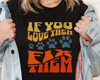 May include: Black t-shirt with a retro-style graphic that says "If you love them fix them" with paw prints and a distressed look.