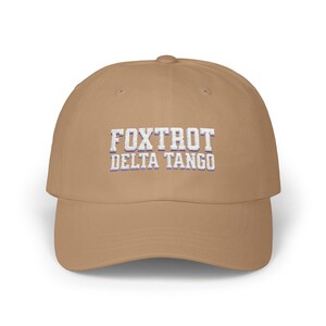 Może przedstawiać: Beżowa czapka z daszkiem z haftowanym białym tekstem "FOXTROT DELTA TANGO".