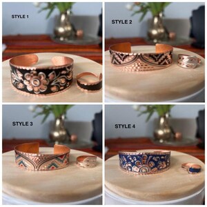 May include: Four different styles of copper bracelets with matching rings. Each bracelet has a unique design with black, blue, and white enamel. The bracelets are displayed on a wooden surface.