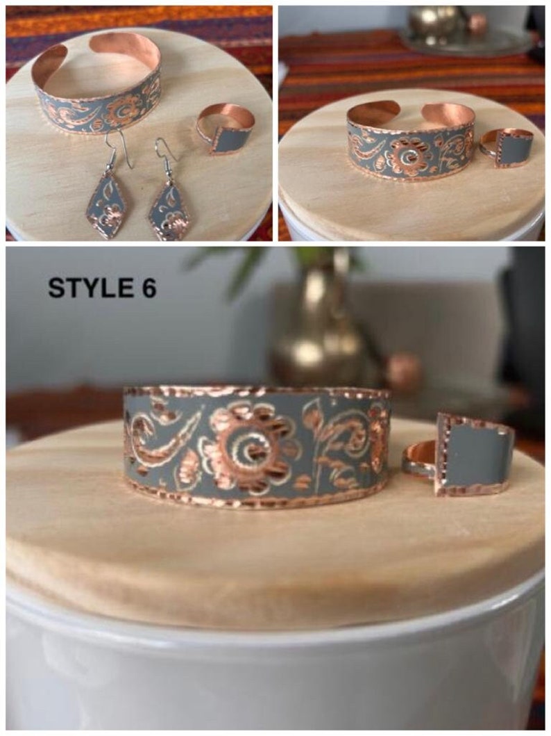 May include: A set of copper jewelry with a gray floral design. The set includes a bracelet, a ring, and a pair of earrings. The jewelry is on a wooden surface. STYLE 6