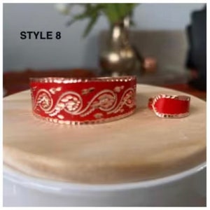 May include: Two red rings with gold trim and a paisley design. The larger ring is wider and has a more intricate design. The smaller ring is plain. The rings are on a white surface. STYLE 8