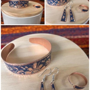 May include: A set of copper jewelry with a blue and copper floral design. The set includes a bracelet, a pair of earrings, and a ring.