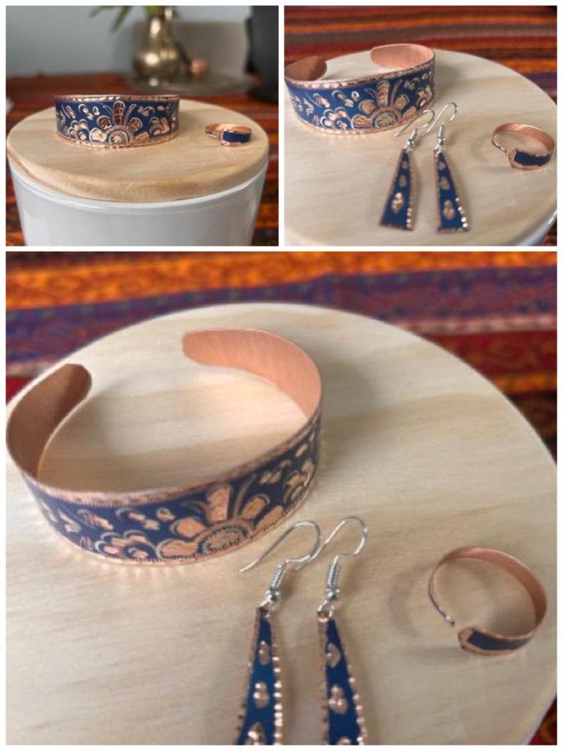 May include: A set of copper jewelry with a blue and copper floral design. The set includes a bracelet, a pair of earrings, and a ring.
