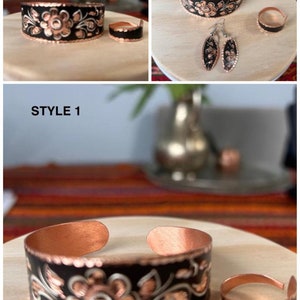 May include: A set of copper jewelry with black enamel and floral designs. The set includes a bracelet, a ring, and a pair of earrings. STYLE 1 is written on the image.