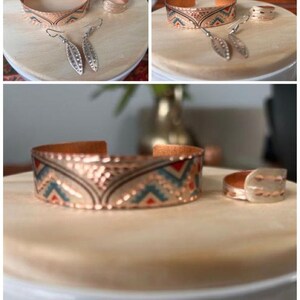 May include: A set of copper jewelry featuring a patterned cuff bracelet, a ring, and a pair of earrings. The jewelry has a geometric design with red, blue, and white accents.