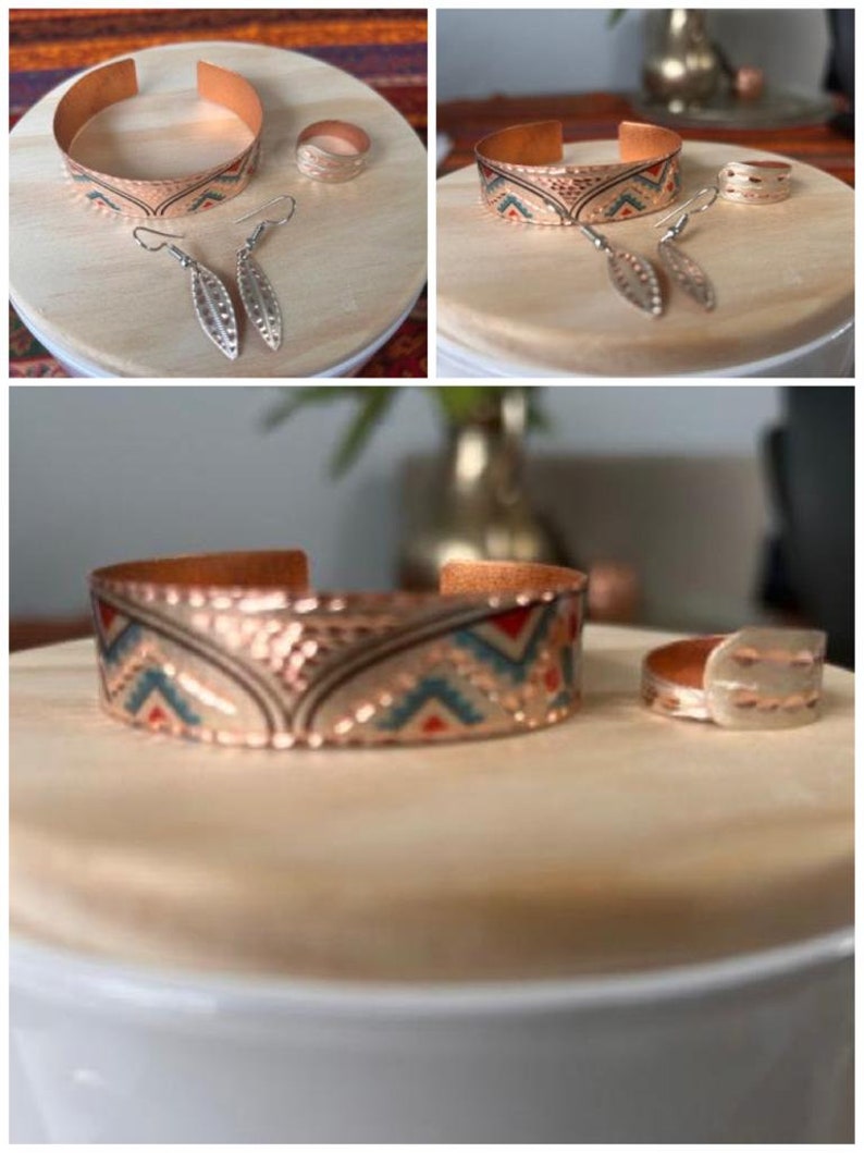 May include: A set of copper jewelry featuring a patterned cuff bracelet, a ring, and a pair of earrings. The jewelry has a geometric design with red, blue, and white accents.