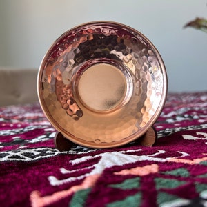 May include: A hammered copper saucer with a shiny finish, resting on a wooden stand. The saucer is a traditional Turkish design, perfect for serving Turkish coffee.