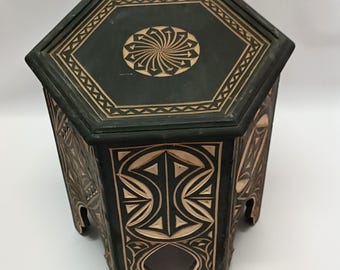 May include: A dark green, hexagonal side table with intricate carved geometric patterns. The tabletop features a central sunburst design. The table is approximately 18 inches wide and 20 inches tall, showcasing a blend of artistry and functionality.