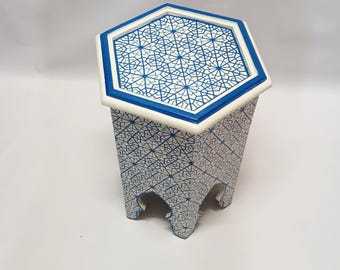 May include: A hexagonal side table with a white and blue geometric pattern. The table has a white border with a blue trim. The legs are cut out in a decorative style. The table is approximately 18 inches tall.
