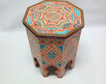 May include: Octagonal wooden stool with intricate geometric patterns painted in shades of orange, pink, blue, green, and gold. The stool has a unique design with arches on the bottom.