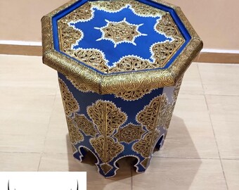 May include: Octagonal wooden table with intricate gold and blue painted designs. The table has a star-shaped design in the center of the top and a decorative base.
