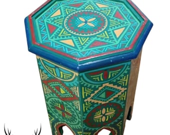 May include: Octagonal wooden table with intricate geometric patterns painted in shades of green, blue, yellow, and red. The table has three legs and a flat top.