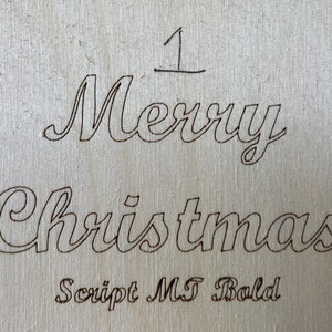 May include: A wood sign with the words "Merry Christmas" written in a cursive font. The font is labeled "Script MT Bold".