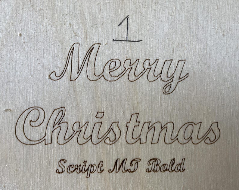 May include: A wood sign with the words "Merry Christmas" written in a cursive font. The font is labeled "Script MT Bold".