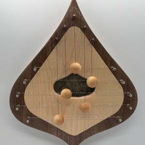 May include: A teardrop-shaped wooden musical instrument with a walnut wood frame and a maple wood soundboard. The instrument has six strings and five wooden balls that hang from the strings. The balls are suspended from the strings by small metal hooks.