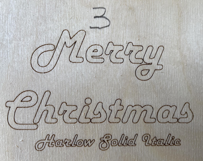 May include: A wood sign with the words "Merry Christmas" in a cursive font. The font is labeled "Harlow Solid Italic".