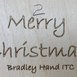 May include: A wooden sign with the text "Merry Christmas" in a handwritten font. The text "Bradley Hand ITC" is also visible below the main text.