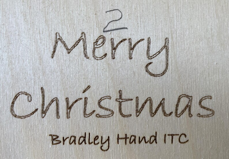 May include: A wooden sign with the text "Merry Christmas" in a handwritten font. The text "Bradley Hand ITC" is also visible below the main text.
