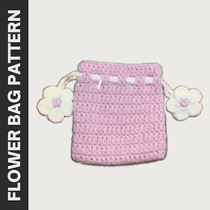 Puede incluir: Un bolso rosa hecho a mano con cierre de cordón y dos adornos de flores. El bolso presenta el texto "FLOWER BAG PATTERN" en el lado izquierdo. El bolso es de color rosa claro.