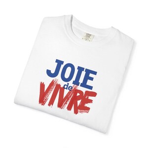 Puede incluir: Una camiseta blanca de manga corta con el texto JOIE de VIVRE impreso en la parte delantera. La palabra JOIE es azul, la palabra de est&aacute; en letras azules peque&ntilde;as y la palabra VIVRE est&aacute; en una fuente roja y negrita estilo pincelada.