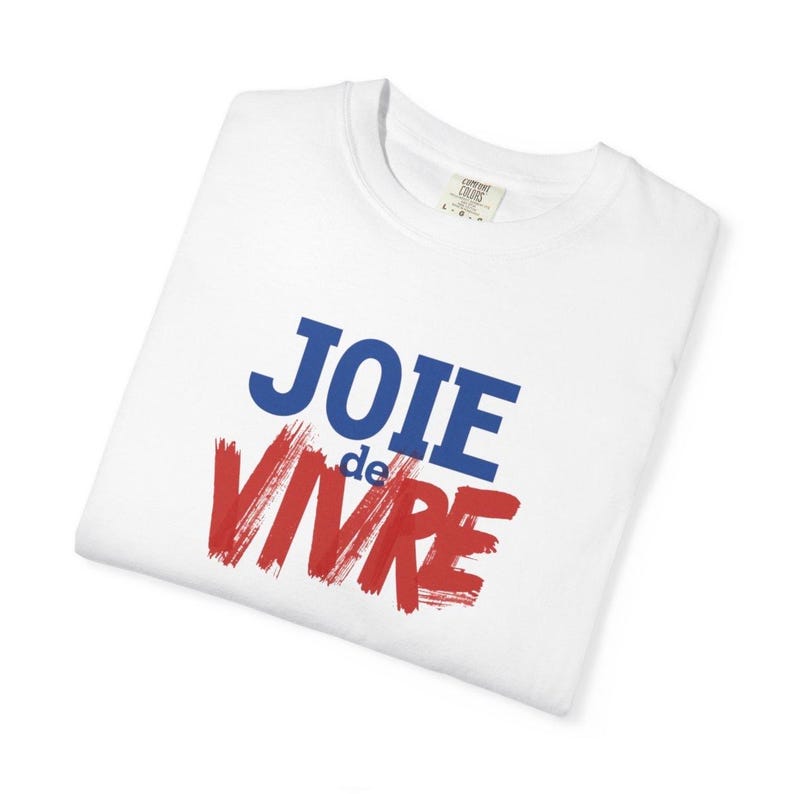Puede incluir: Una camiseta blanca de manga corta con el texto JOIE de VIVRE impreso en la parte delantera. La palabra JOIE es azul, la palabra de est&aacute; en letras azules peque&ntilde;as y la palabra VIVRE est&aacute; en una fuente roja y negrita estilo pincelada.