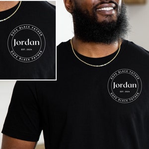 Puede incluir: Una camiseta negra con un gráfico circular blanco que dice "Dope Black Father (Jordan) Est. 2024"