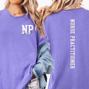 May include: A lilac sweatshirt featuring the text "NP Sarah" in white on the front. The back of the sweatshirt displays the words "NURSE PRACTITIONER" in white, printed vertically. A denim jacket is partially visible.