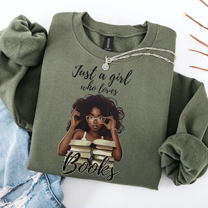 Op de afbeelding: Een groen sweatshirt met de tekst "Just a girl who loves books" en een illustratie van een zwarte vrouw met een bril die een stapel boeken vasthoudt.