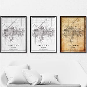 May include: Three framed maps of Champaign, Illinois, in black frames. The maps have a detailed street layout. The first map is grayscale, the second is black and white, and the third has a sepia tone. Each map includes the city name and coordinates.