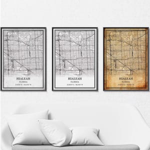 May include: Three framed maps of Hialeah, Florida, in black frames. The maps have a detailed street layout. One map is in grayscale, another in black and white, and the third has a sepia tone. Each map includes the city name and coordinates.