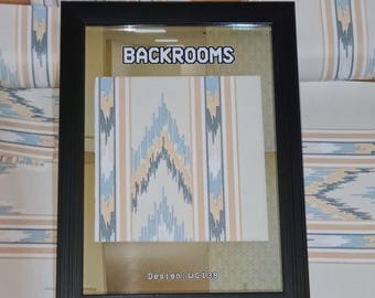 May include: A framed wallpaper sample with a black frame. The wallpaper features a repeating geometric pattern in shades of blue, beige, and gray. The text "BACKROOMS" is displayed above the sample, and "Design: WC138" is below.