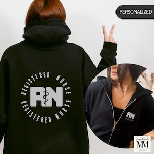 May include: Black hooded sweatshirt with a white graphic that says "Registered Nurse Registered" with a caduceus symbol and the letters "RN" in the centre. The sweatshirt is shown on a model wearing it with the hood up.