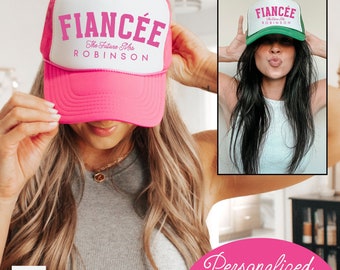 May include: Pink and white trucker hat with the text "Fiancée The Future Mrs. ROBINSON" in pink letters. The hat is being worn by a person with long brown hair. The image also shows a green and white trucker hat with the text "Fiancée The Future Mrs. ROBINSON" in black letters. The image has the text "Personalized Add your name" at the bottom.